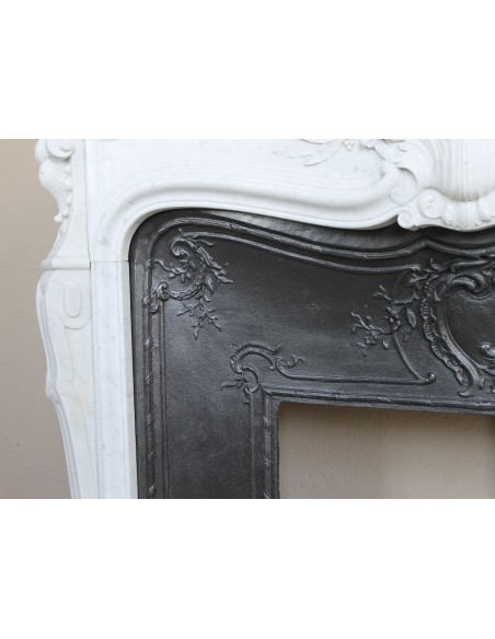 A refined antique white marble mantel in the Baroque style, carved with floral motifs, with its original cast iron insert.