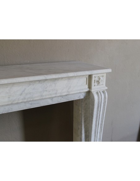 Small and well-proportioned Neoclassical fireplace with curved shoulders in white marble, an elegant and refined fire surround.