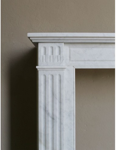 Neoclassical "Marguerite" fireplace in White Carrara marble, featuring a finely carved central floral motif and fluted capitals.