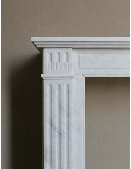 Neoclassical "Marguerite" fireplace in White Carrara marble, featuring a finely carved central floral motif and fluted capitals.