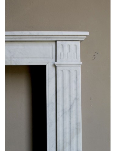 Neoclassical "Marguerite" fireplace in White Carrara marble, featuring a finely carved central floral motif and fluted capitals.
