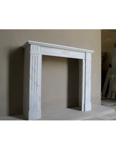 Neoclassical "Marguerite" fireplace in White Carrara marble, featuring a finely carved central floral motif and fluted capitals.