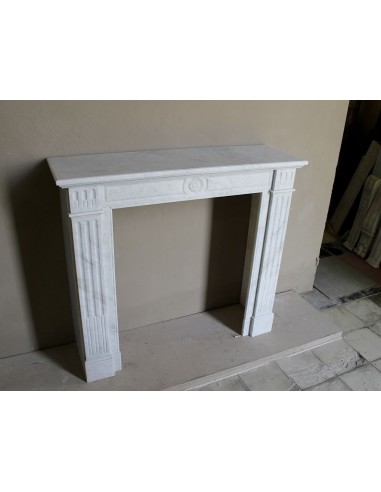Neoclassical "Marguerite" fireplace in White Carrara marble, featuring a finely carved central floral motif and fluted capitals.