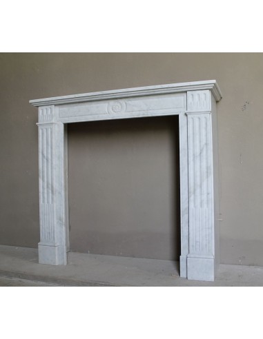 Neoclassical "Marguerite" fireplace in White Carrara marble, featuring a finely carved central floral motif and fluted capitals.