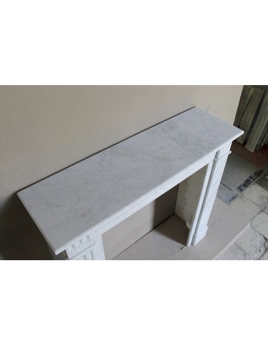 Neoclassical "Marguerite" fireplace in White Carrara marble, featuring a finely carved central floral motif and fluted capitals.