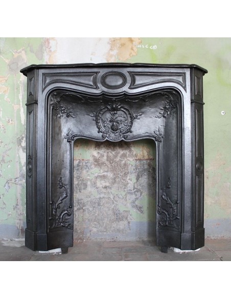 Antique cast-iron fireplace mantel with floral decorations, with a pomegranate casting in the center of the frieze.